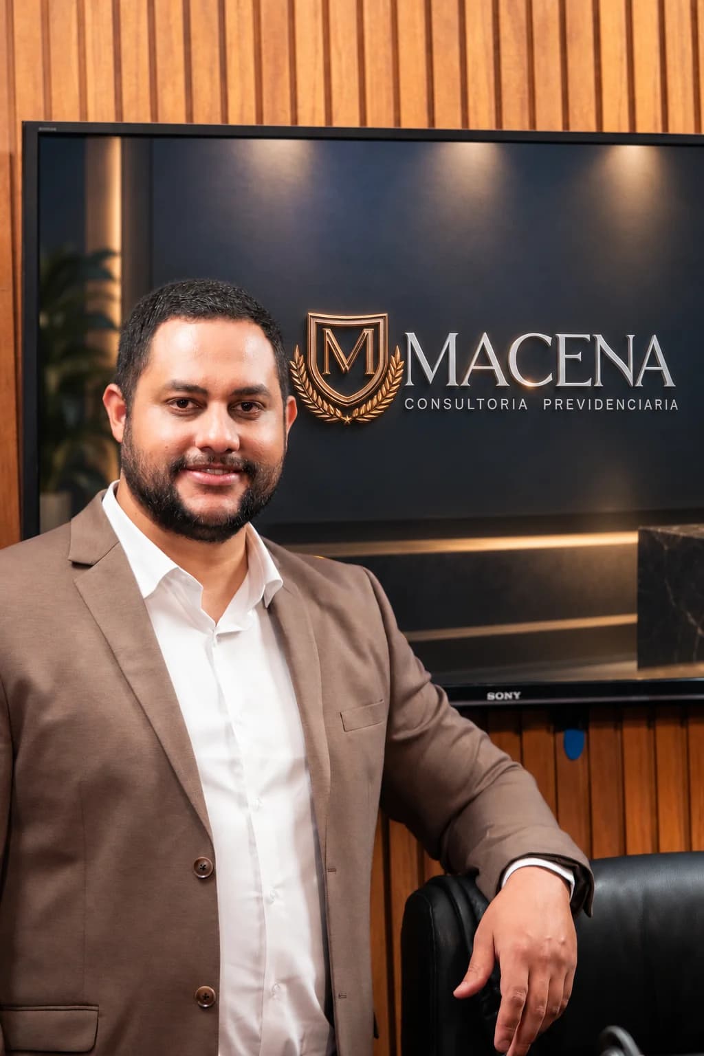 Macena no estúdio, com a marca Macena Consultoria Previdenciária no telão ao fundo